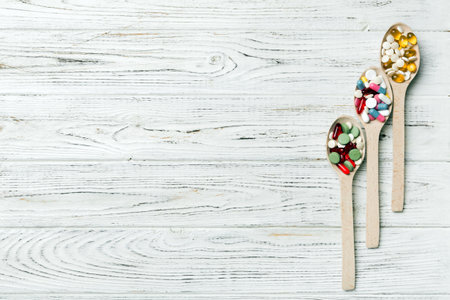 Vitamin capsules in a wooden spoon on a colored background. Pills served as a healthy meal. Drugs, pharmacy, medicine or medical healthycare concept.の写真素材