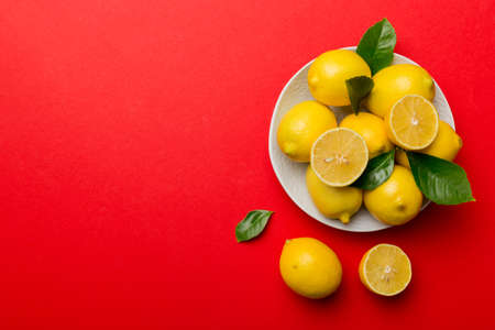 Fresh cutted lemon and whole lemons over round plate on colored background. Food and drink ingredients preparing. healthy eating theme top view with copy space.の写真素材