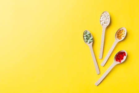 Top view Variety of vitamin and mineral pills in wooden spoon on Colored background. Top view of...