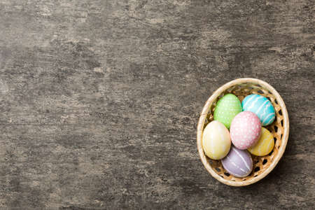 Multi colors Easter eggs in the woven basket on colored background . Pastel color Easter eggs....