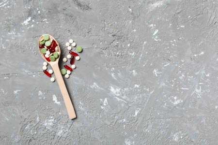 Vitamin capsules in a wooden spoon on a colored background. Pills served as a healthy meal. Drugs, pharmacy, medicine or medical healthycare concept.の写真素材