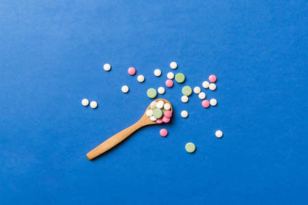 Vitamin capsules in a wooden spoon on a colored background. Pills served as a healthy meal. Drugs, pharmacy, medicine or medical healthycare concept.の写真素材