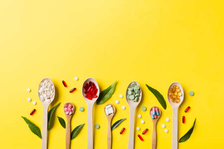 Top view Variety of vitamin and mineral pills in wooden spoon on Colored background. Top view of...