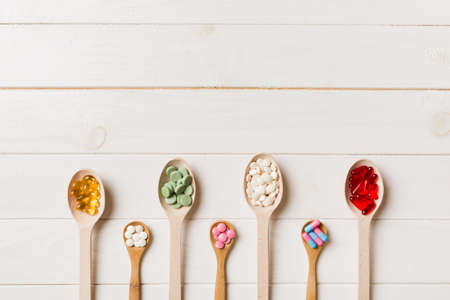 Top view Variety of vitamin and mineral pills in wooden spoon on Colored background. Top view of...