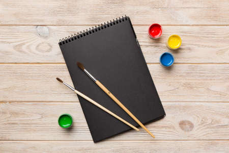 Album pages and paints, pencils, brush on a colored background. Top view with empty space. workplace for creativity. home teaching concept drawing.の写真素材