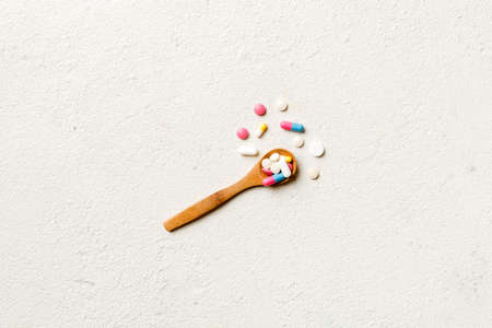 Vitamin capsules in a wooden spoon on a colored background. Pills served as a healthy meal. Drugs, pharmacy, medicine or medical healthycare concept.の写真素材