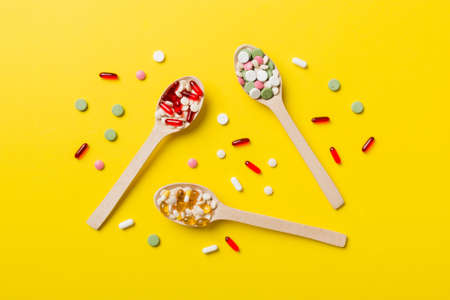 Vitamin capsules in a wooden spoon on a colored background. Pills served as a healthy meal. Drugs,...