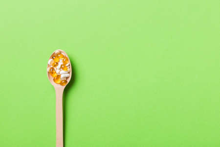 Vitamin capsules in a wooden spoon on a colored background. Pills served as a healthy meal. Drugs, pharmacy, medicine or medical healthycare concept.の写真素材