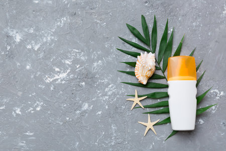 Sunscreen spray bottle. Bottle with sun protection cream and sea shells with tropical green leaf on color background, top view.の写真素材