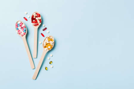 Vitamin capsules in a wooden spoon on a colored background. Pills served as a healthy meal. Drugs, pharmacy, medicine or medical healthycare concept.の写真素材