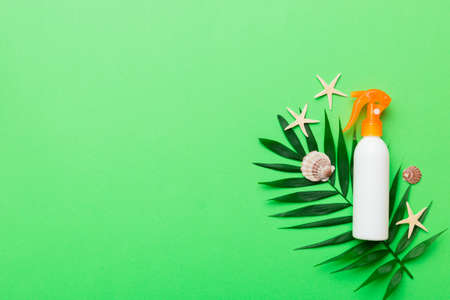 Sunscreen spray bottle. Bottle with sun protection cream and sea shells with tropical green leaf on color background, top view.の写真素材