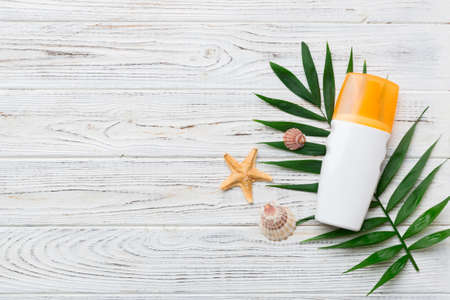Sunscreen spray bottle. Bottle with sun protection cream and sea shells with tropical green leaf on color background, top view.の写真素材