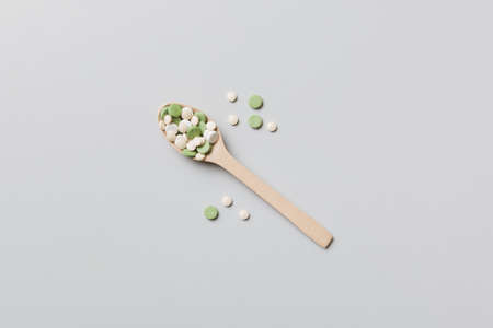 Vitamin capsules in a wooden spoon on a colored background. Pills served as a healthy meal. Drugs, pharmacy, medicine or medical healthycare concept.の写真素材