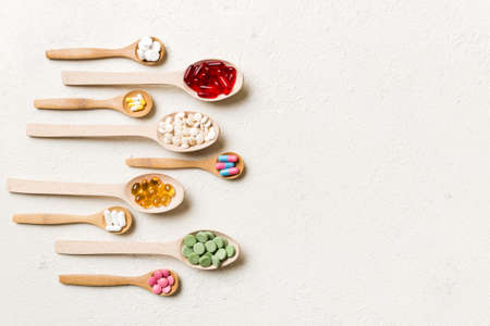 Top view Variety of vitamin and mineral pills in wooden spoon on Colored background. Top view of assorted pharmaceutical medicine pills. Dietary supplement healthcare product.の写真素材