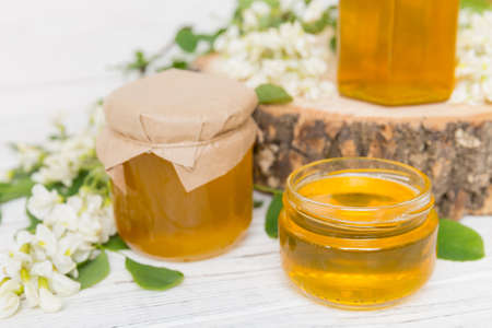 Sweet honey jar surrounded by spring acacia blossoms. Honey flows from a spoon in a jar. jars of...