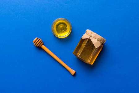 Glass jar of honey with wooden drizzler on colored background. Honey pot and dipper high above. Top view copy space.の写真素材