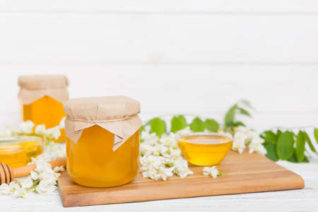 Sweet honey jar surrounded by spring acacia blossoms. Honey flows from a spoon in a jar. jars of clear fresh acacia honey on wooden background.の写真素材