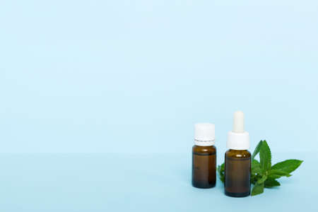 Natural Mint Essential Oil in a Glass Bottle. organic cosmetics with herbal extracts of mint on colored background.の写真素材