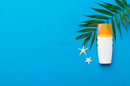 Sunscreen spray bottle. Bottle with sun protection cream and sea shells with tropical green leaf on...