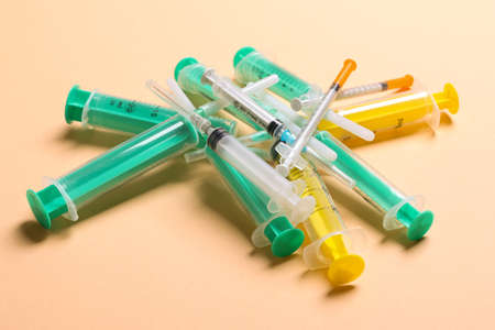 Top view of a pile of medical syringes and insulin syringes with needles at orange background with copy space. Injection treatment concept.の写真素材