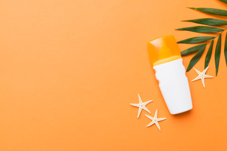 Sunscreen spray bottle. Bottle with sun protection cream and sea shells with tropical green leaf on color background, top view.の写真素材