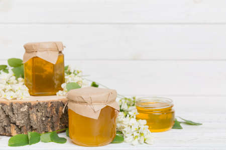 Sweet honey jar surrounded by spring acacia blossoms. Honey flows from a spoon in a jar. jars of clear fresh acacia honey on wooden background.の写真素材