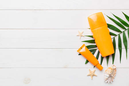 Sunscreen spray bottle. Bottle with sun protection cream and sea shells with tropical green leaf on color background, top view.の写真素材