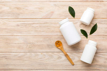 Omega-3 capsules lie in white bottle on a table with green leaves background. fish oil tablets....