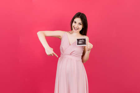 Cute Pregnant Lady Posing With Baby Sonography Photo Near Colored background. Concept of pregnancy, gynecology, medical test, maternal health.の写真素材