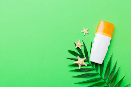 Sunscreen spray bottle. Bottle with sun protection cream and sea shells with tropical green leaf on color background, top view.の写真素材