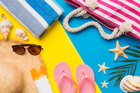 Beach accessories straw hat and seashell on colored table. Summer concept background.