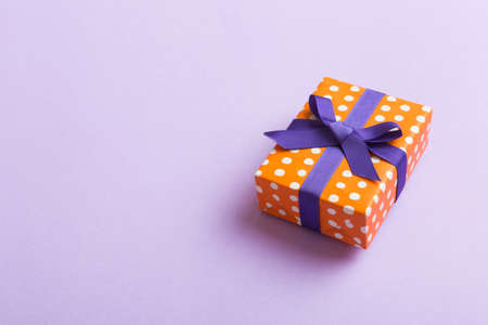wrapped Christmas or other holiday handmade present in paper with purple ribbon on colored background. Present box, decoration of gift on colored table, top view with copy space.の写真素材