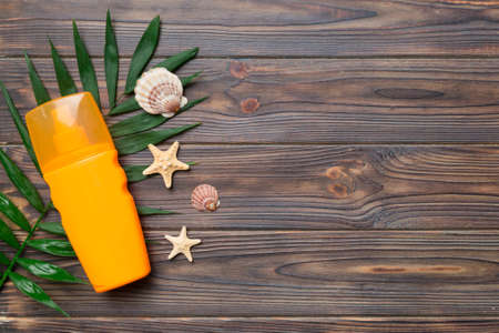 Sunscreen spray bottle. Bottle with sun protection cream and sea shells with tropical green leaf on...