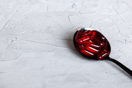 Vitamin capsules in a spoon on a colored background. Pills served as a healthy meal. Red soft gel vitamin supplement capsules on spoon.の写真素材