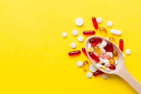 Vitamin capsules in a spoon on a colored background. Pills served as a healthy meal. Red soft gel vitamin supplement capsules on spoon.の写真素材