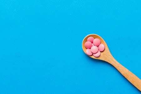 Vitamin capsules in a spoon on a colored background. Pills served as a healthy meal. Red soft gel vitamin supplement capsules on spoon.の写真素材