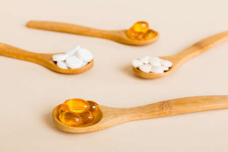 Vitamin capsules in a spoon on a colored background. Pills served as a healthy meal. Red soft gel vitamin supplement capsules on spoon.の写真素材