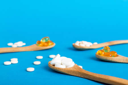 Vitamin capsules in a spoon on a colored background. Pills served as a healthy meal. Red soft gel...