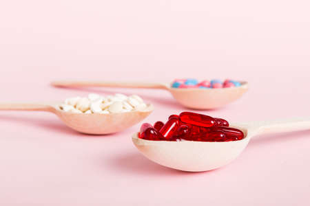 Vitamin capsules in a spoon on a colored background. Pills served as a healthy meal. Red soft gel...