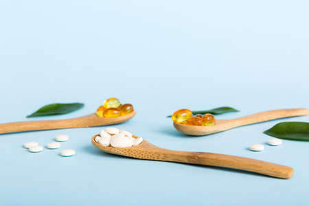 Vitamin capsules in a spoon on a colored background. Pills served as a healthy meal. Red soft gel vitamin supplement capsules on spoon.の写真素材