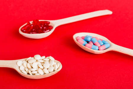 Vitamin capsules in a spoon on a colored background. Pills served as a healthy meal. Red soft gel...