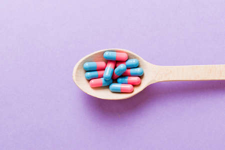 Vitamin capsules in a spoon on a colored background. Pills served as a healthy meal. Red soft gel vitamin supplement capsules on spoon.の写真素材