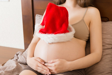 Pregnant in santa hat holding her belly. Christmas and New Year concept.の写真素材