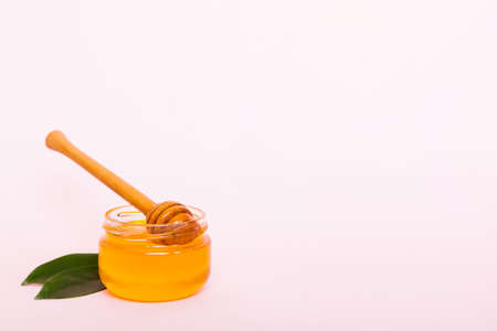 Honey in jar with leaves and honey dipper on colored background top view with copy text.