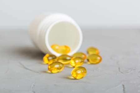 Soft gels pills with Omega-3 oil spilling out of pill bottle close-up. Gel capsule bottles white surface. Omega 3, multivitamins, Calcium, antibiotics. health. immunity.の写真素材