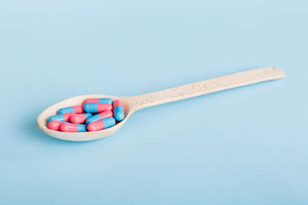 Vitamin capsules in a spoon on a colored background. Pills served as a healthy meal. Red soft gel...