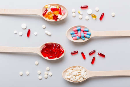 Vitamin capsules in a spoon on a colored background. Pills served as a healthy meal. Red soft gel vitamin supplement capsules on spoon.の写真素材