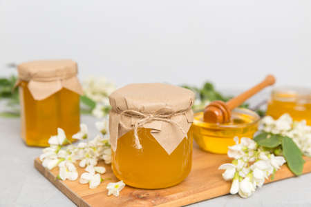 Sweet honey jar surrounded by spring acacia blossoms. Honey flows from a spoon in a jar. jars of...