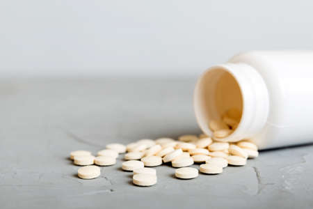 Medicine bottle and white pills spilled on a light background. Medicines and prescription pills flat lay background. White medical pills and tablets spilling out of a drug bottle.の写真素材