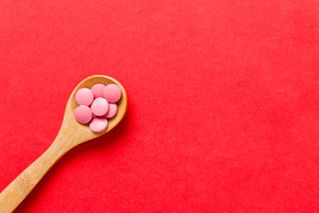 Vitamin capsules in a spoon on a colored background. Pills served as a healthy meal. Red soft gel vitamin supplement capsules on spoon.の写真素材